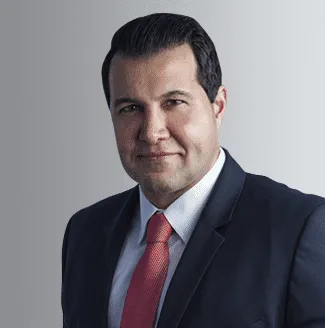 Professional man in a suit with a red tie posing against a neutral gray background looking confidently at the camera suitable for business or corporate themes.